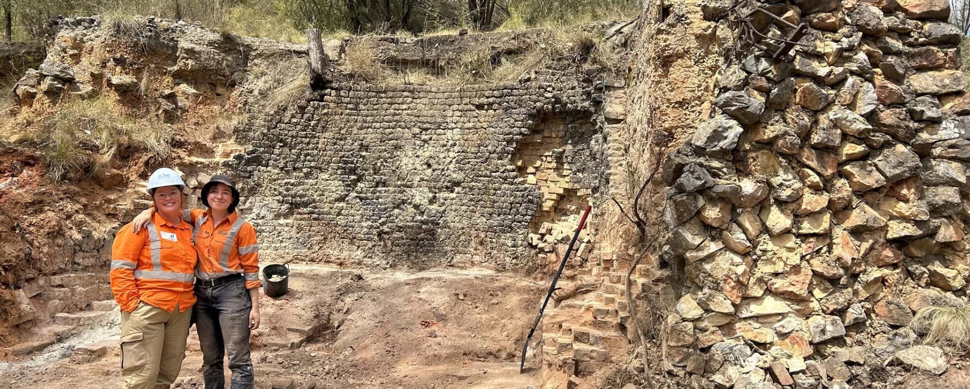 Two females at an archaeology work site with arms around shoulder